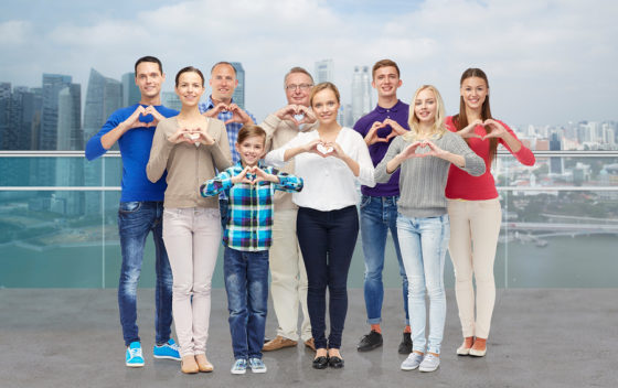 group of smiling men, women and boy showing heart shape hand sign